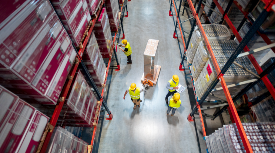 Warehouse workers at work between rows of tall shelves full of packed boxes, top view